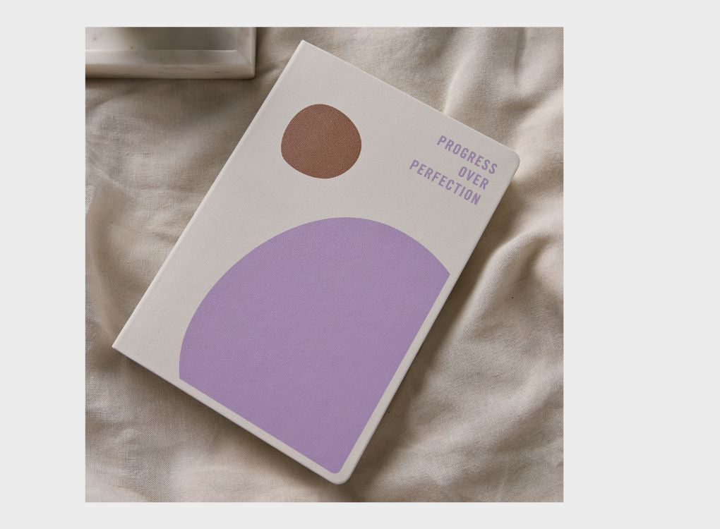 2026 Daily Goal Digger Diary in Progress over perfection. White cover with abstract shapes against a soft natural background.