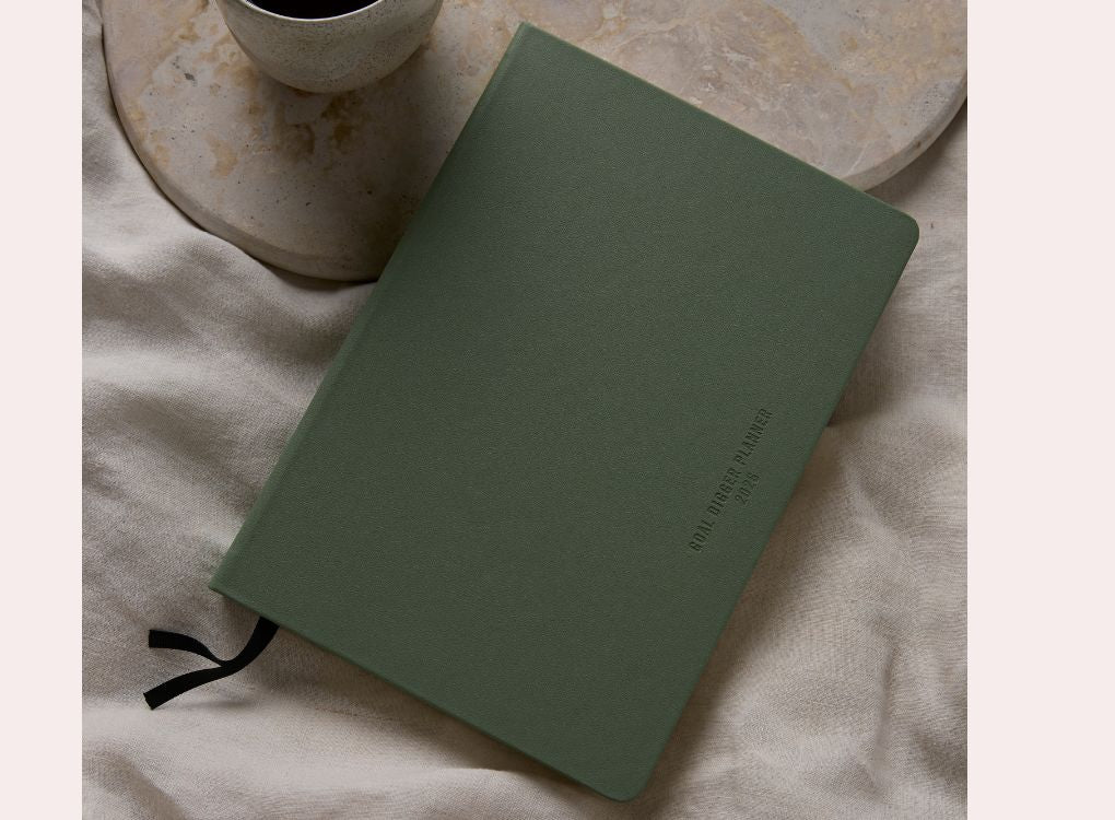 MiGoals 2026 Classic Diary in sea green with embossed “Goal Digger Planner 2026” on the cover, styled on a stone tray with a coffee cup and fabric backdrop.