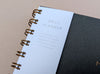 Daily planner with gold spiral binding on a beige background